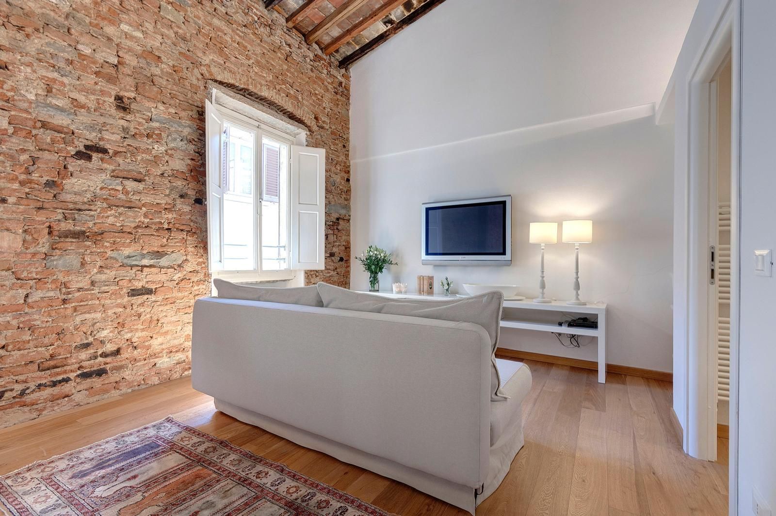 A room with a white sofa, a television, a lamp, and a brick wall.