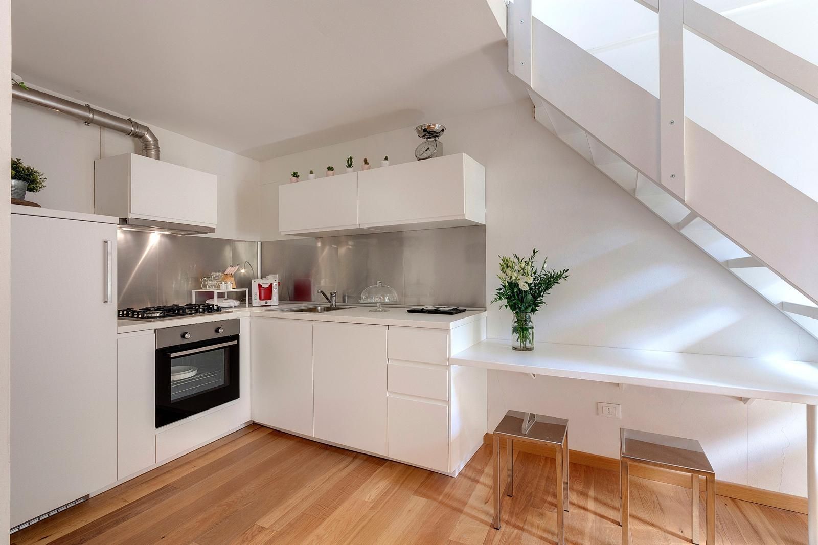 Une cuisine moderne avec des meubles blancs, un four encastré, une hotte en acier inoxydable et un plancher en bois.