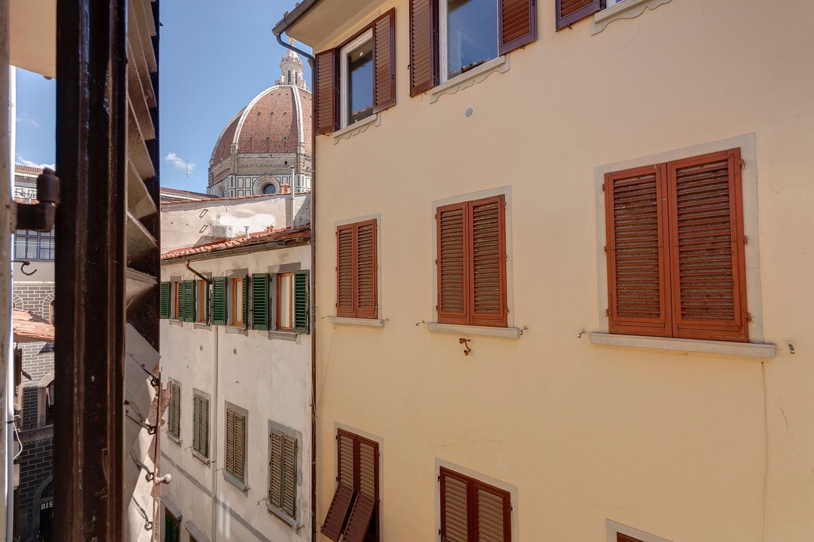 Ein Gebäude mit mehreren Fenstern, einige mit Fensterläden, und einer Kuppel im Hintergrund.