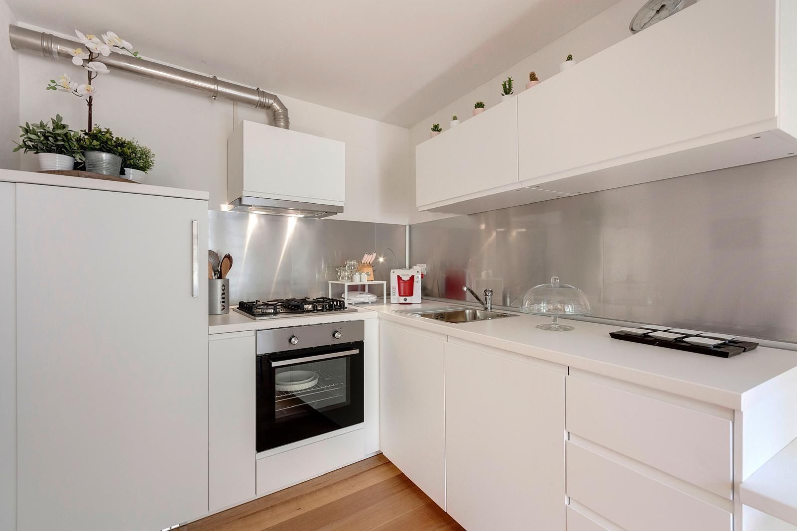 A modern kitchen with white cabinetry, a built-in oven, a gas stove, and a stainless steel sink.
