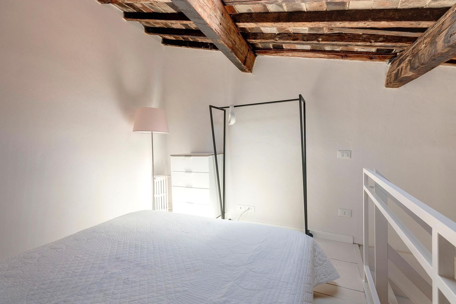 A bedroom with a bed, a bedside lamp, a radiator, and a wooden ceiling.