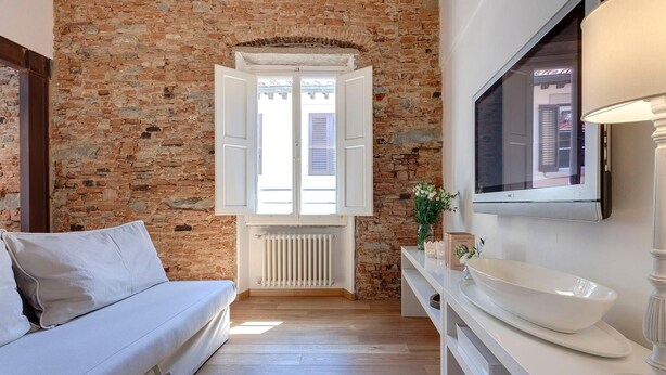 Ein Zimmer mit Backsteinwand, einem weißen Sofa, einem weißen Waschtisch mit Spüle und einem an der Wand montierten Fernseher.
