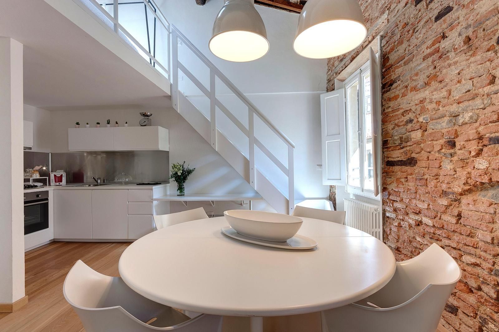 Une cuisine moderne avec des meubles blancs et un mur en briques.