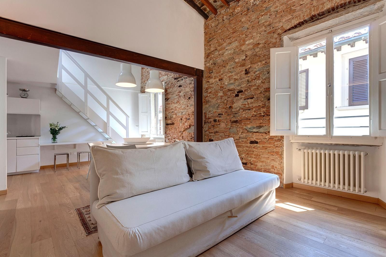 A modern living room with a white sofa, a brick wall, and a staircase leading to an upper floor.