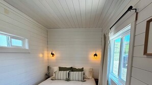 Een slaapkamer met een bed, twee wandlampen, een raam en een houten vloer.