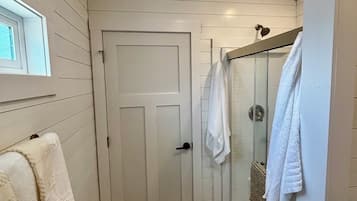 A narrow bathroom with a wooden floor, a white door, and a glass shower enclosure.