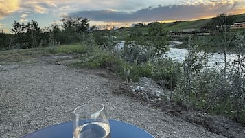 Een hand die een wijnglas vasthoudt op een blauwe tafel, met uitzicht op een rivier en heuvels.