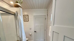 Een badkamer met een houten vloer, witte wanden, een douche en een deur.