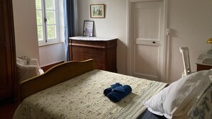 Een slaapkamer met een bed, een kapstok, een deur en een raam met gordijnen.