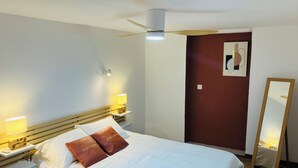 Hotellihuone, jossa on sänky, yöpöytälamput, kattotuuletin, seinään kiinnitetty valaisin, peili ja ovi, jonka yhteydessä on punaisella värillä korostettu seinä.