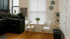Cocina compacta con microondas, cafetera y plantas en macetas. Se observa una mesa de comedor con sillas y un cesto de basura.