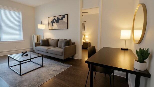 Een moderne woonkamer met een bank, salontafel en een eettafel. Aan de muur hangt een schilderij, er staat een lamp en een pot met een plant.