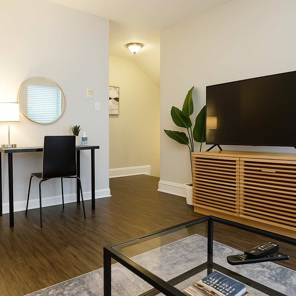 Uma sala de estar moderna com televisão de tela plana, mesa de centro de vidro, cadeira preta, armário de madeira e escrivaninha com cadeira.