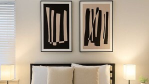 Een verzorgde hotelkamer met een groot bed, twee bedlampen en twee abstracte kunstwerken aan de muur.