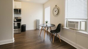Een moderne keuken met inbouwapparatuur, een eethoek met een ronde tafel en twee stoelen, en een raam met zonwering.