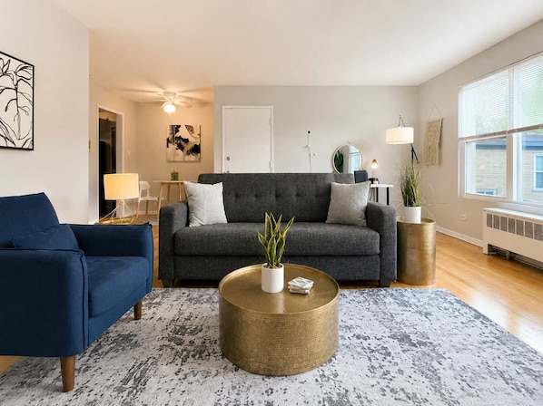 A living room with a dark grey sofa, a blue armchair, a round coffee table with a plant, and a patterned rug.