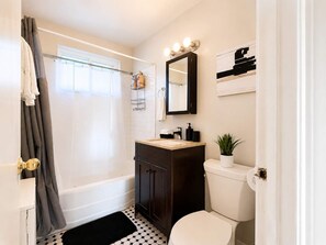 A bathroom with a bathtub, toilet, sink, and a mirror with lights. - Bright & Cozy Chicago 1BR | Near Dining & Transit (Chicago)