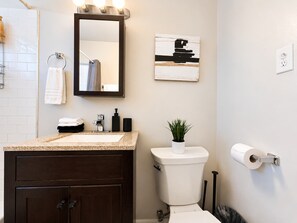 A bathroom with a sink, mirror, toilet, and a wall-mounted light fixture.