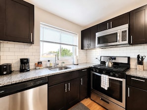 A modern kitchen with dark cabinets, a stainless steel range, a microwave, a dishwasher, and a window with blinds.