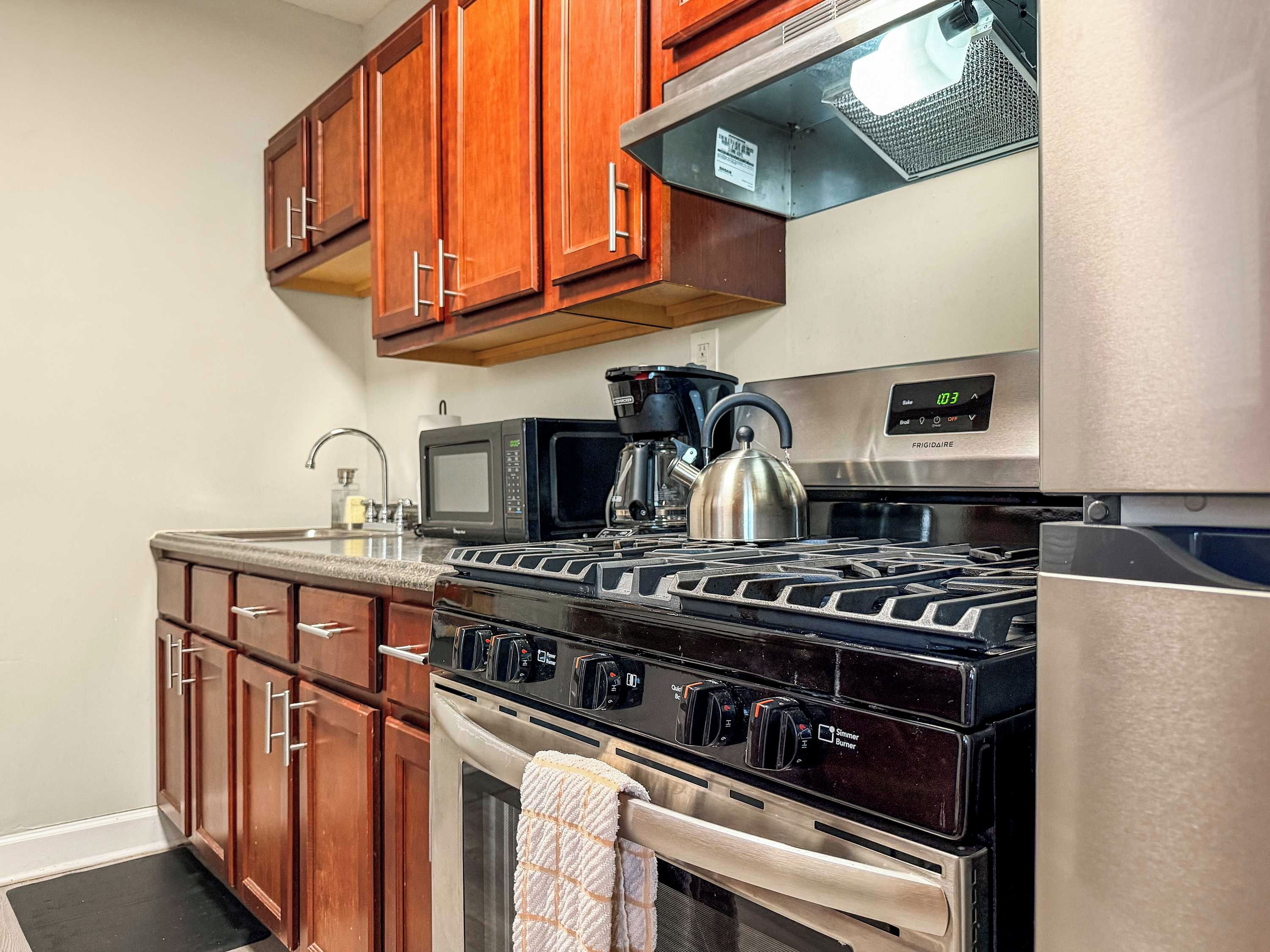 Una cocina con armarios de madera, estufa de acero inoxidable, microondas y refrigerador.
