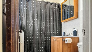 A bathroom with a wooden cabinet, a toilet, a sink with a soap dispenser, and a shower curtain with a pattern. - Chic, Quiet 1BR Near Dining Options– Perfect for 2 (Chicago)