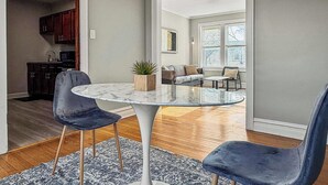 A modern living room with a marble coffee table, two blue velvet chairs, a potted plant, and a view of a kitchen and dining area through an open doorway. - Chic, Quiet 1BR Near Dining Options– Perfect for 2 (Chicago)