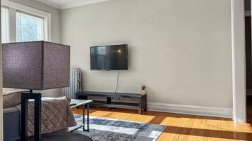 A modern living room with a flat-screen TV mounted on the wall, a dark-colored sofa, a small table, and a patterned rug on a wooden floor.