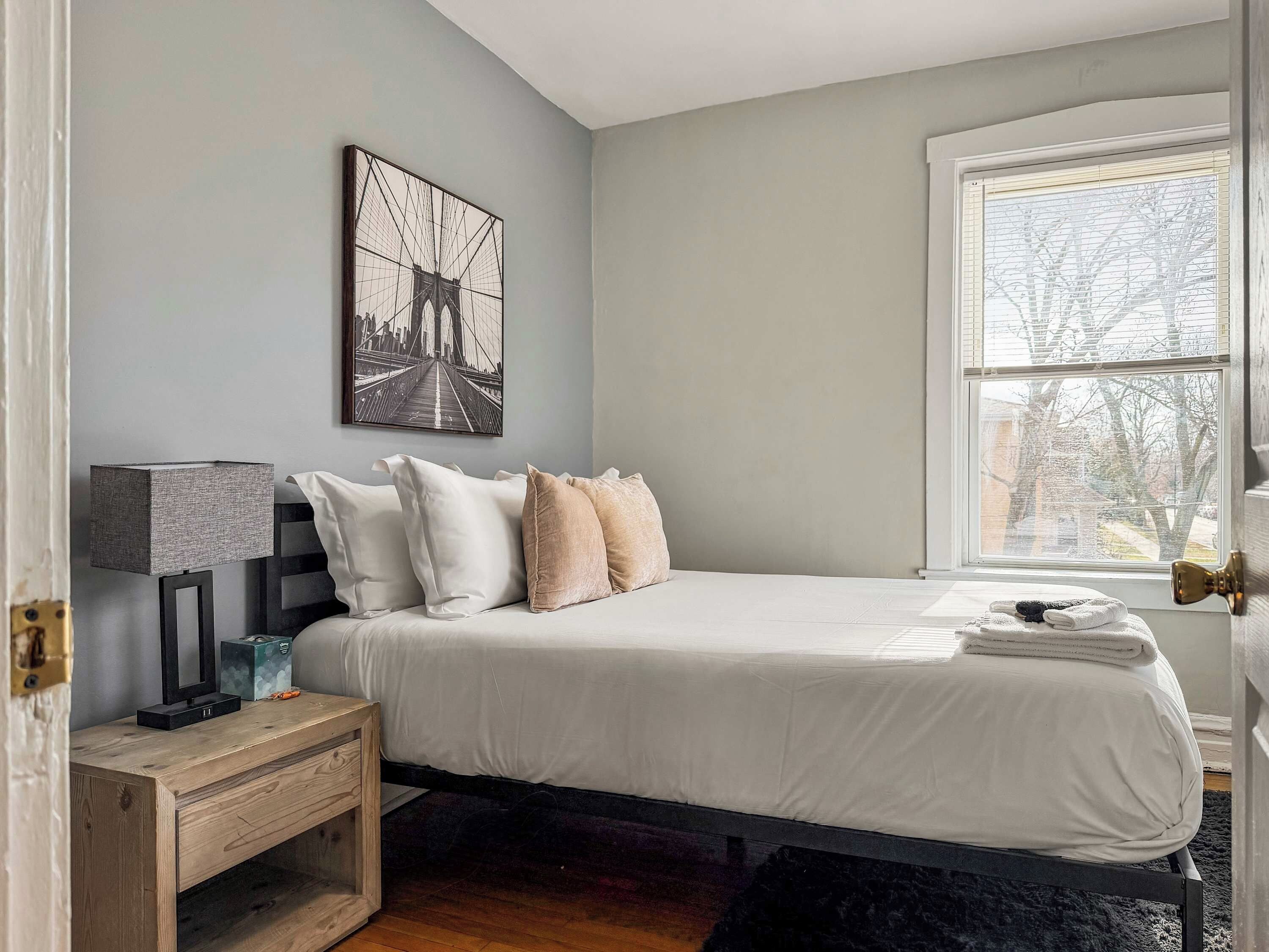 Un dormitorio con cama, mesita de noche, lámpara y ventana con vista a árboles.