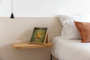 A neatly made bed with a white pillow and a brown throw. A wooden nightstand holds a book titled 'X COLLECTOR' by NERI. - Luxury boutique hotel with ocean views and a beach within walking distance (Pietrosella)