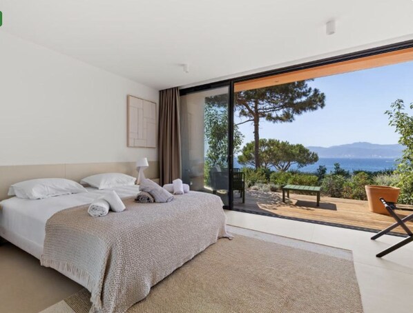 Un dormitorio con una cama grande, vistas al exterior y una banca afuera.