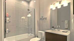 Un baño moderno con ducha envuelta en vidrio, un inodoro blanco y un tocador con espejo y lavabo.