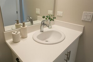A bathroom with a white sink, a mirror, and a faucet. There are two rolls of toilet paper and a small vase with green leaves on the counter. - Modern Studio on Broadway (Chicago)
