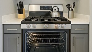 Cozinha com fogão, forno de aço inoxidável e armários cinzas.