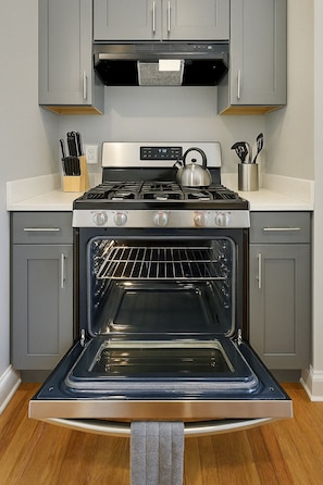 A kitchen with a stainless steel stove, oven, and grey cabinets. - Modern Studio on Broadway (Chicago)