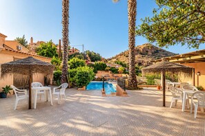 Ein Poolbereich mit Liegestühlen und Sonnenschirmen, umgeben von Palmen und einer Bergkulisse.