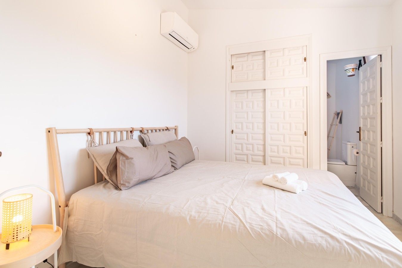A bedroom with a bed, pillows, a bedside table with a lamp, and a wardrobe.