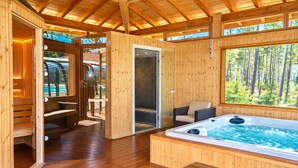 Eine Holzhütte mit Whirlpool, Sitzgelegenheit und Blick auf den Wald.