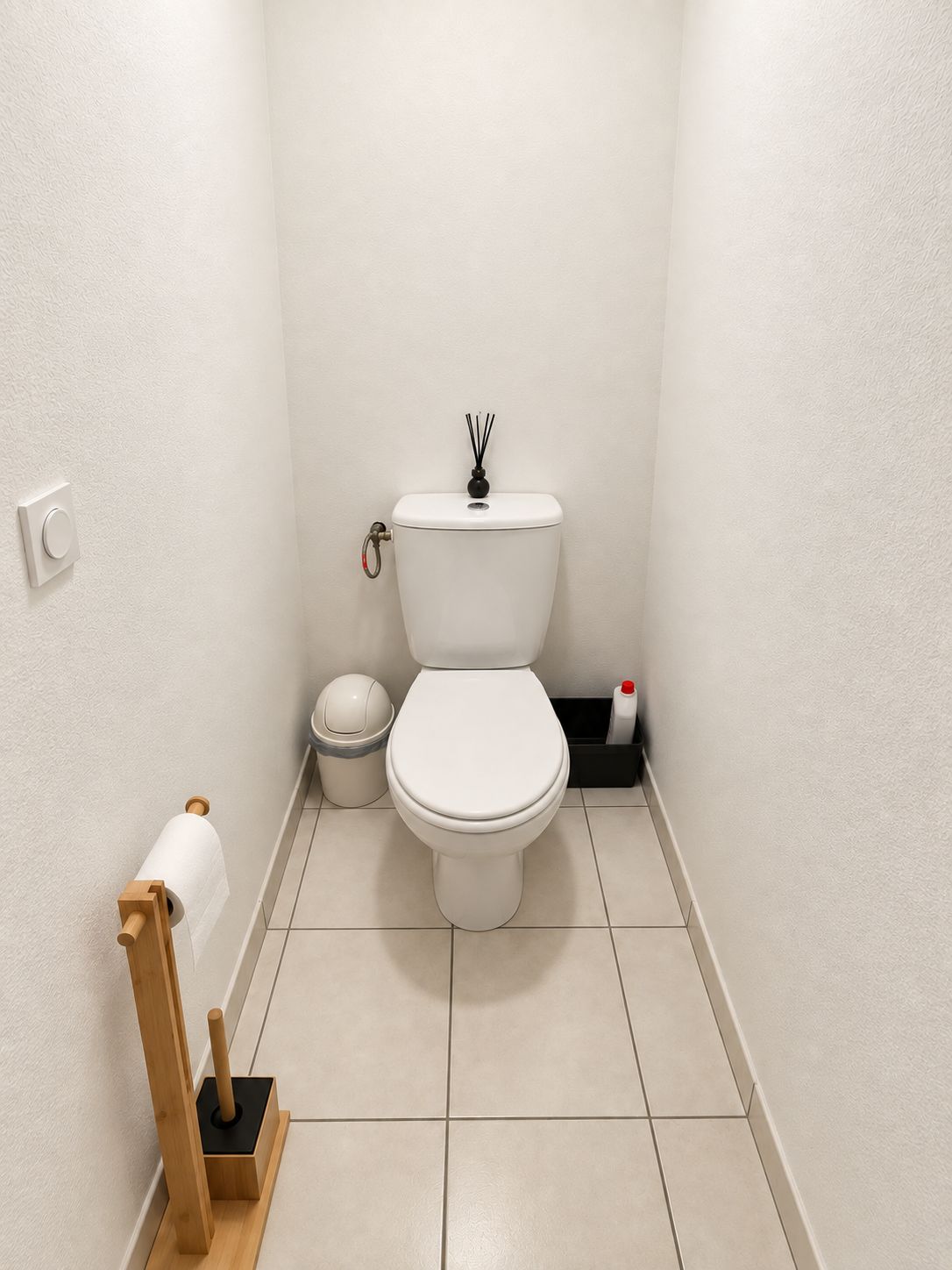 A small, clean bathroom with a toilet, a trash bin, a toilet paper holder, and a bottle of hand sanitizer.