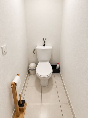 A small, clean bathroom with a toilet, a trash bin, a toilet paper holder, and a bottle of hand sanitizer. - Villa for 6 people at Domaine des Grands Lacs – Pools & Lake (Parentis-en-Born)
