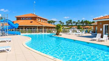 A swimming pool with a slide, lounge chairs, and a building with a red roof.