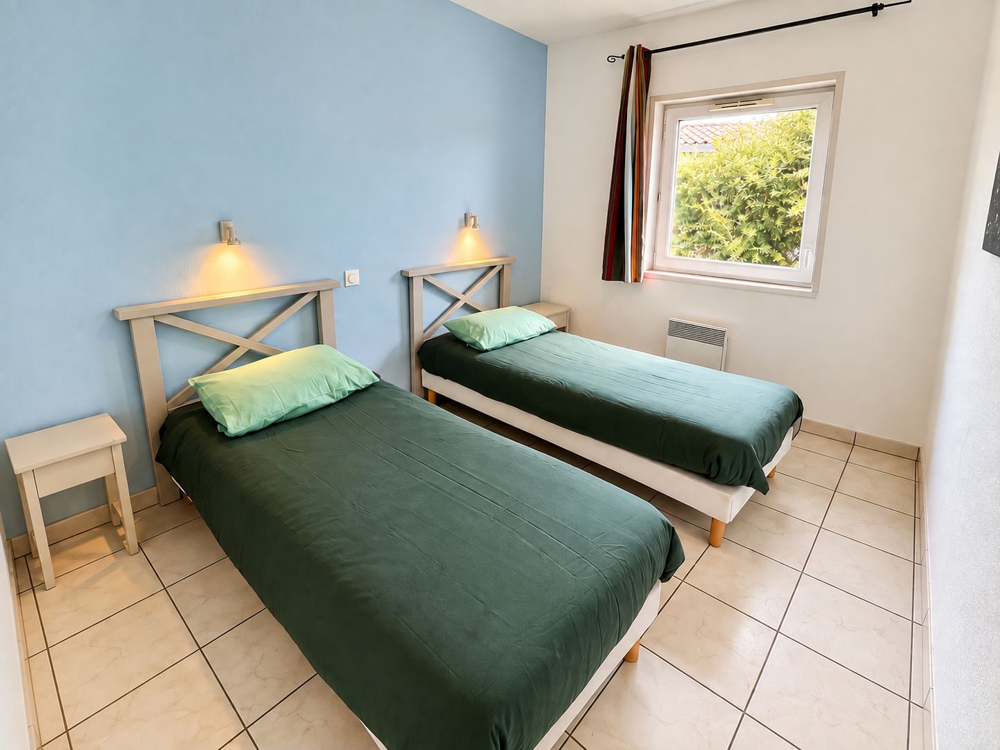 A room with two single beds, a window with a view of greenery, and a radiator.