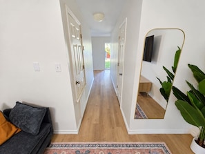 A hallway with a sofa, a mirror, and a plant. - Stay Local | Starkville 2BR near MSU (Starkville)