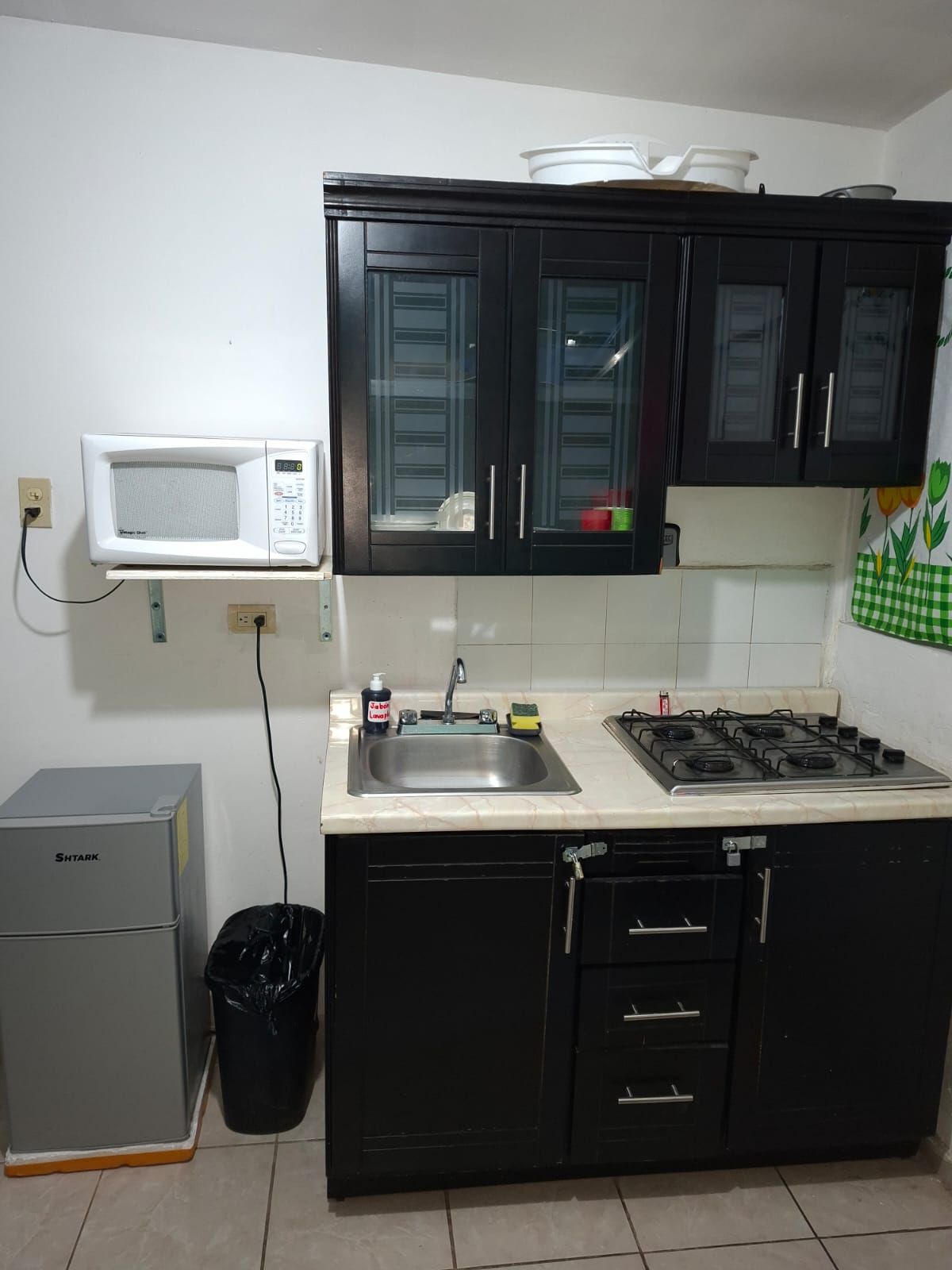 Een keuken met een magnetron, spoelbak, fornuis, kasten en een prullenbak.