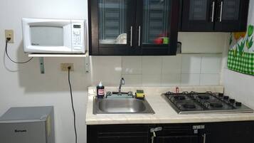 Een keuken met een magnetron, spoelbak, fornuis, kasten en een prullenbak.