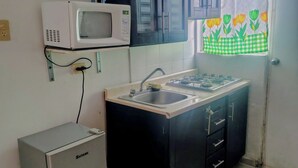Une cuisine de taille réduite équipée d’un four à micro-ondes, d’une cuisinière à gaz et d’un réfrigérateur.