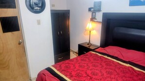 Une chambre à coucher comprenant un lit, une armoire, une table de chevet avec une lampe et une étagère fixée au mur.