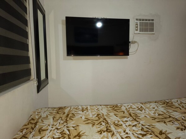 A room with a bed, a television mounted on the wall, and a window with blinds.
