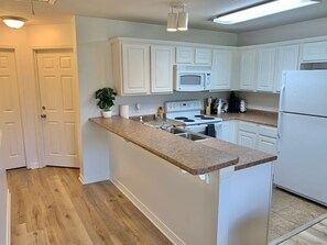 A kitchen with white cabinets, a microwave, a stove, and a refrigerator. - Reel Retreat near MSU 2 BED (Starkville)
