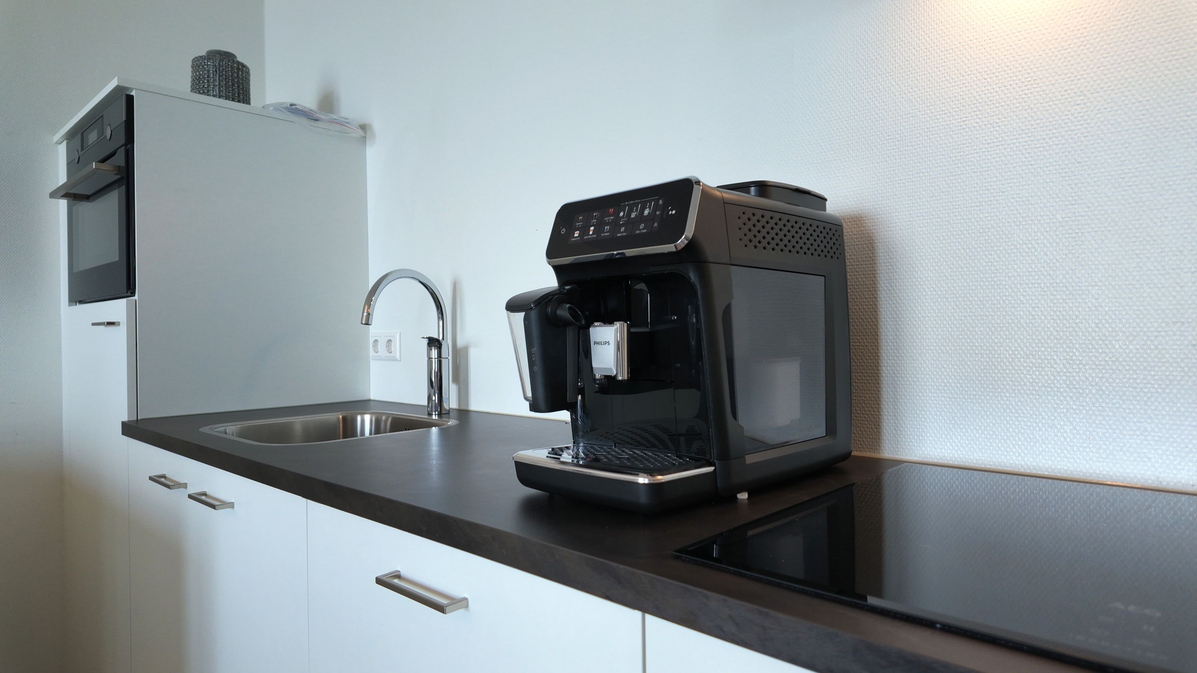 A modern kitchen with a built-in coffee maker, a stainless steel sink, and a microwave.