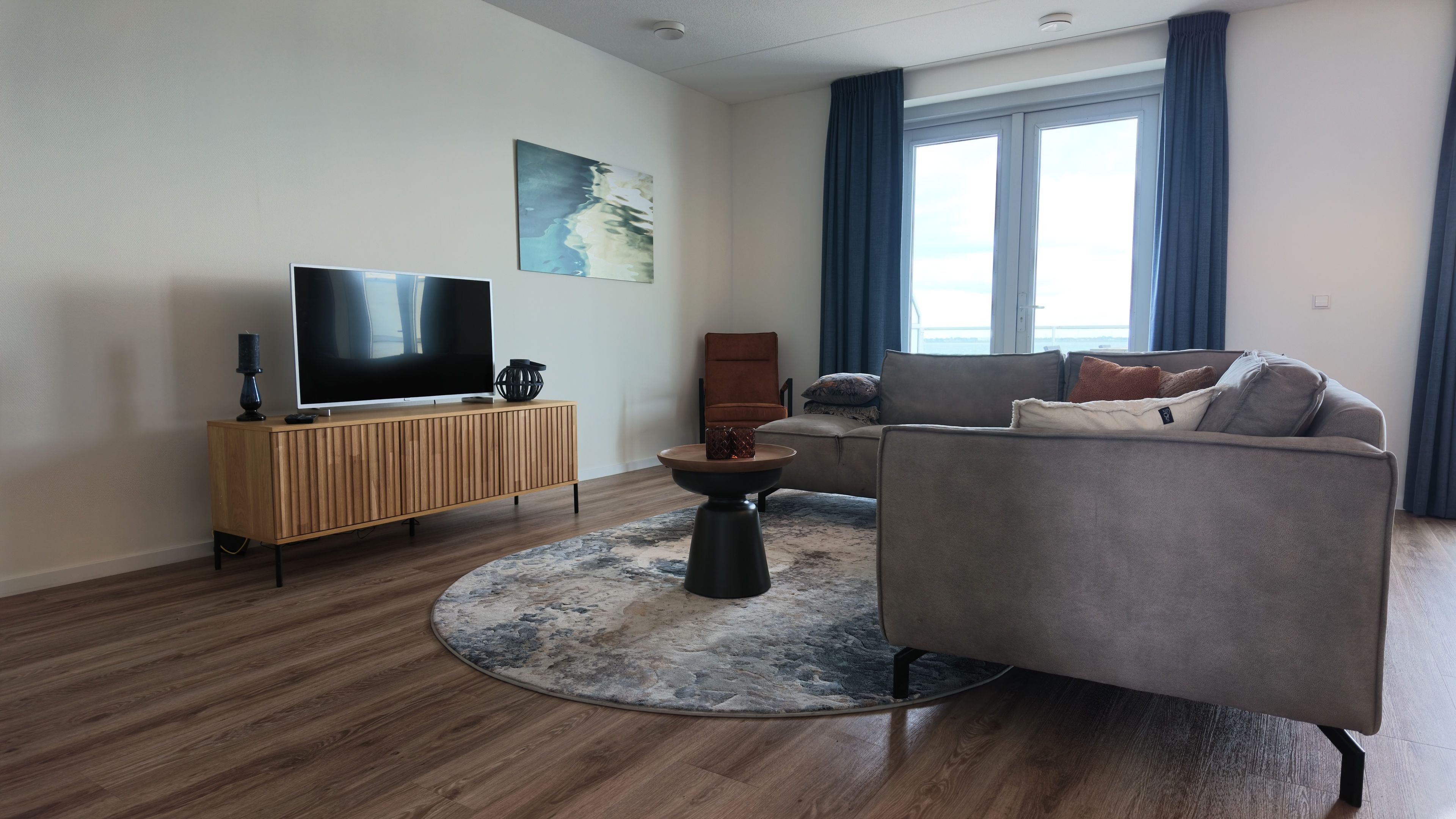 A modern living room with a flat-screen TV, a wooden cabinet, a grey sofa, and a round coffee table.